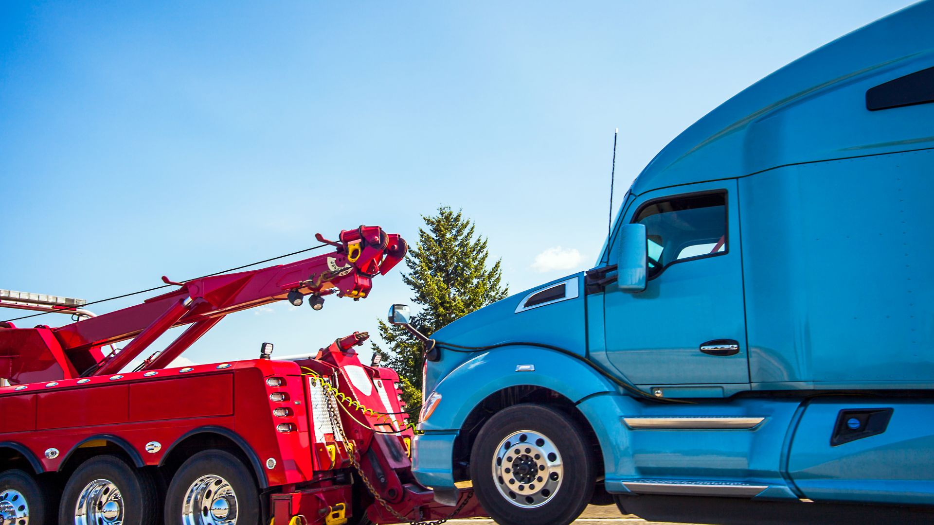 Red tow truck preparing to haul blue semi-truck on sunny day
