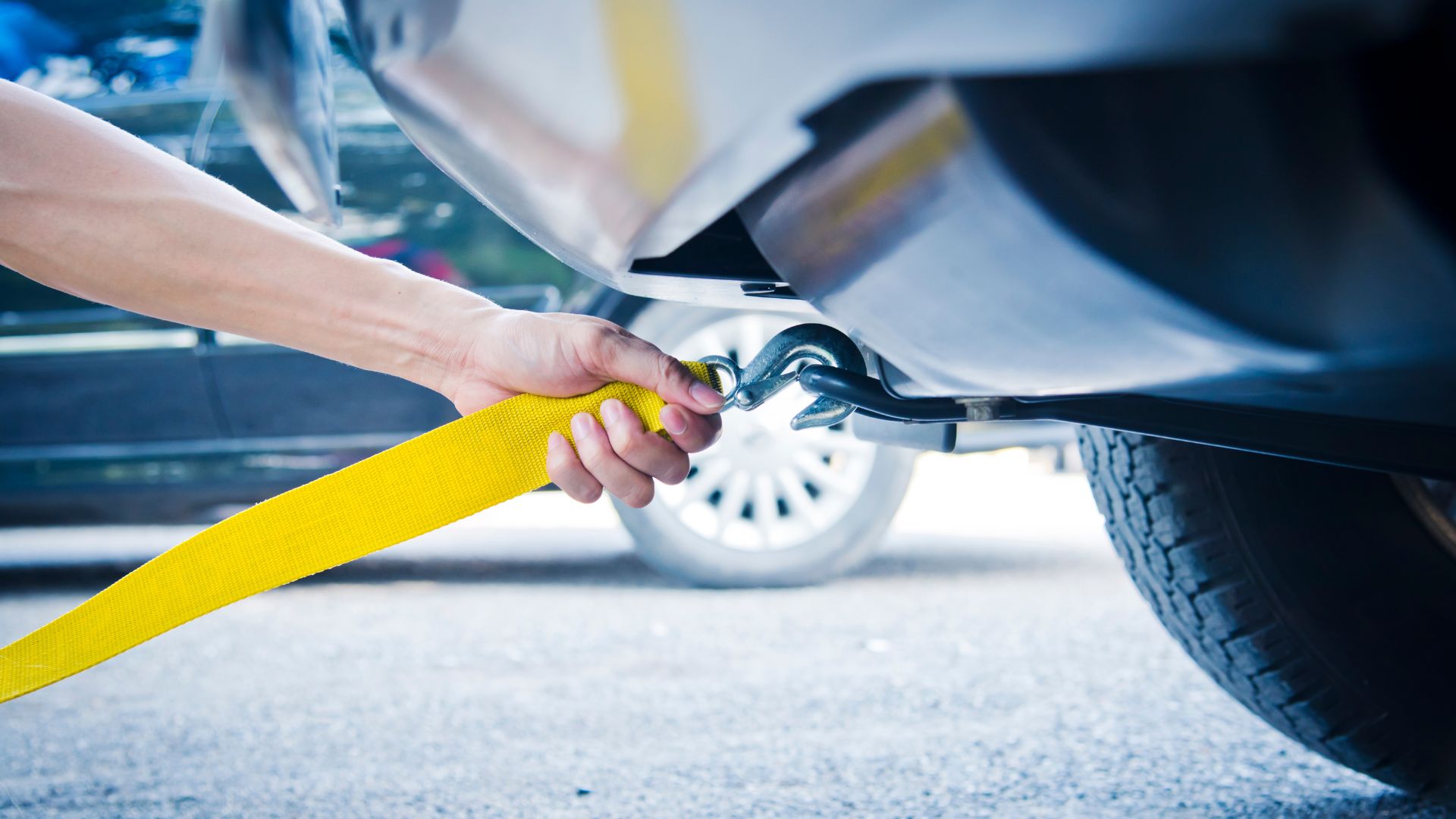 Hand holding yellow tow strap connecting to car's towing hook